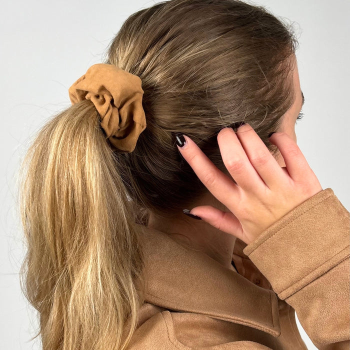 Woman with long blonde hair in a ponytail, wearing a tan jacket and tan suedette scrunchie.