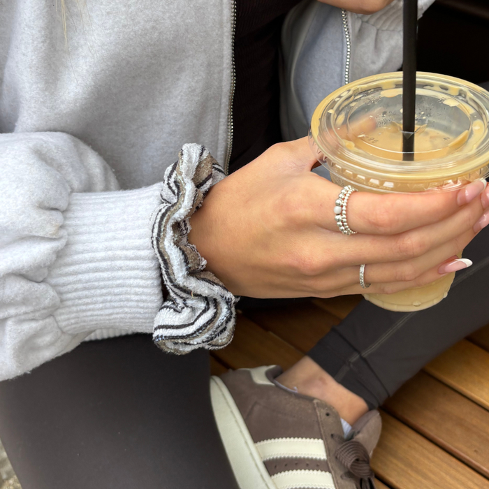 Hand with a Retro Stripes Coconut Lane TOWEL scrunchie and gray sleeve holds iced coffee at a wooden table.