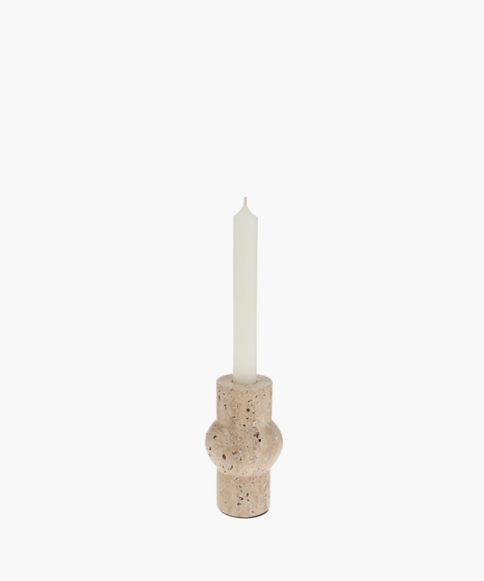 A tall white candle in a rounded, beige travertine stone holder with a textured surface. The minimalist design evokes a calm and serene atmosphere. | SW Home