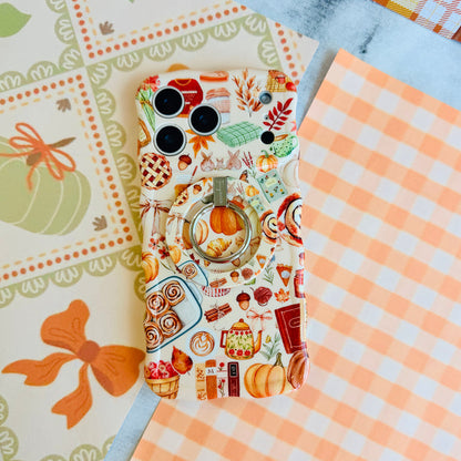 All The Fall Things MagSafe grip ring attached to the matching All The Fall Things iPhone case, styled on orange gingham and a pumpkin illustration backdrop.