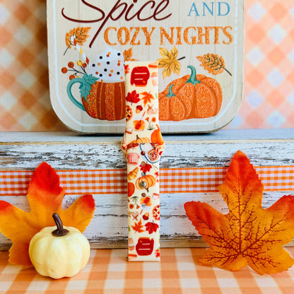All The Fall Things Samsung Galaxy Watch band single strap half standing on weathered wood beside a white pumpkin, showing the watercolor collage print and quick-release end.