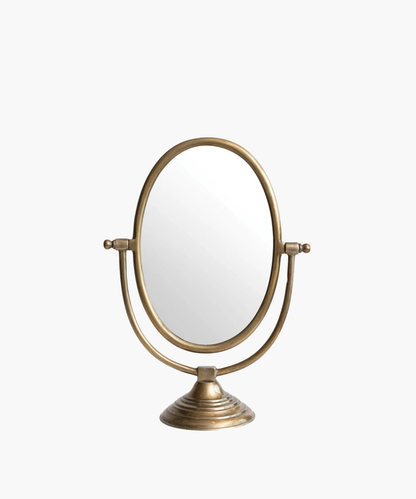 A vintage-style tabletop mirror with an oval shape and bronze finish. It features an adjustable frame resting on a decorative, circular base. | Wildwood Home Co.