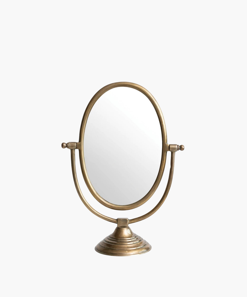 A vintage-style tabletop mirror with an oval shape and bronze finish. It features an adjustable frame resting on a decorative, circular base. | Wildwood Home Co.