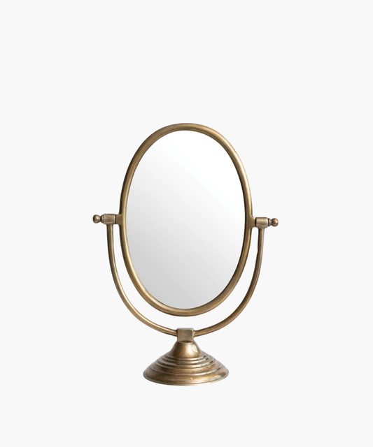 A vintage-style tabletop mirror with an oval shape and bronze finish. It features an adjustable frame resting on a decorative, circular base. | Wildwood Home Co.