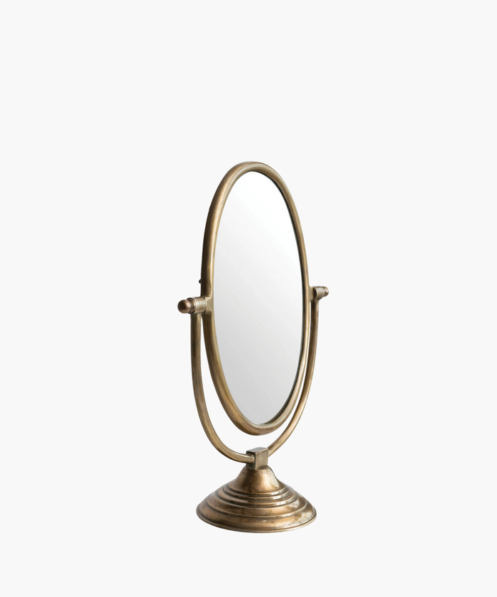 A vintage-style tabletop mirror with an oval shape and bronze finish. It features an adjustable frame resting on a decorative, circular base. | Wildwood Home Co.