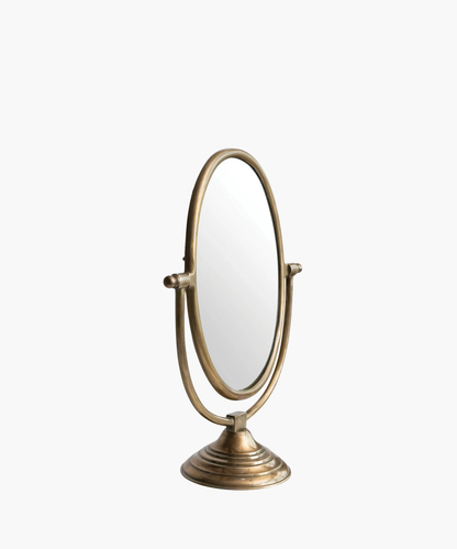 A vintage-style tabletop mirror with an oval shape and bronze finish. It features an adjustable frame resting on a decorative, circular base. | Wildwood Home Co.