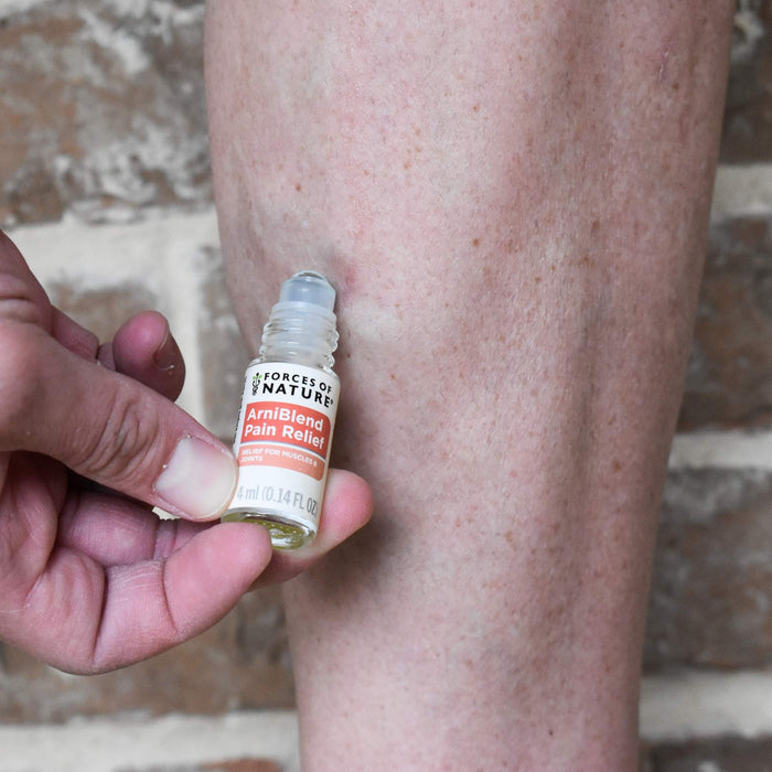 Hand holding ArniBlend Pain Relief 4 ml roll-on showing label and roller applicator, applied to a leg