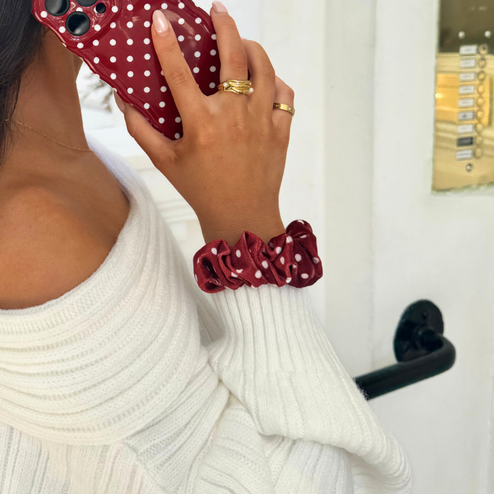 Woman with a burgundy polka dot scrunchie holds a matching red phone case.