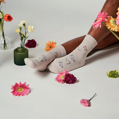 Beige half cushion socks with butterfly designs, surrounded by colorful flowers on a white surface.