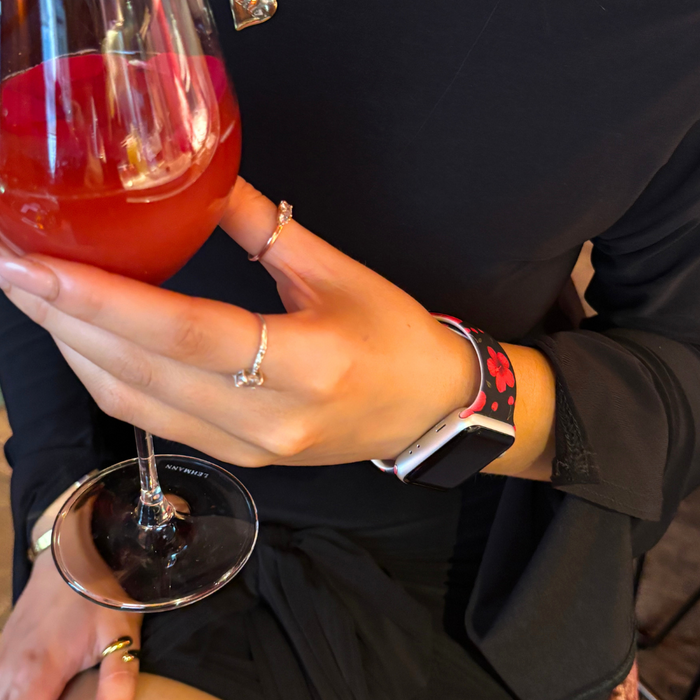 Person in black with rings holds a red drink, wearing a pink floral Apple Watch strap from Coconut Lane.