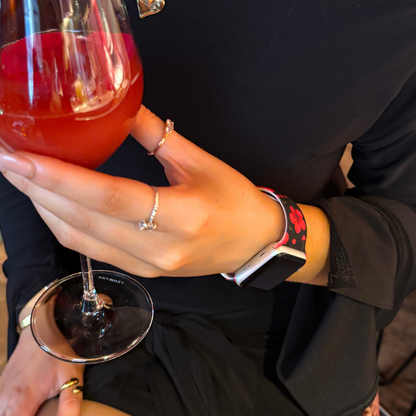 Person in black with rings holds a red drink, wearing a pink floral Apple Watch strap from Coconut Lane.