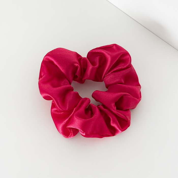 Cherry red scrunchie with a smooth finish by Coconut Lane on a white surface near a wall corner.