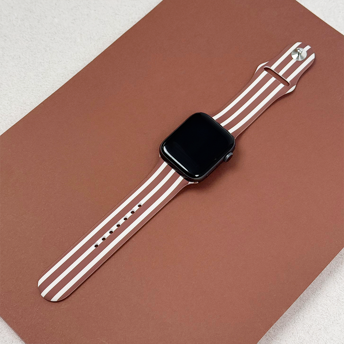 Coconut Lane Apple Watch strap with chestnut brown stripes on a brown rectangular surface.