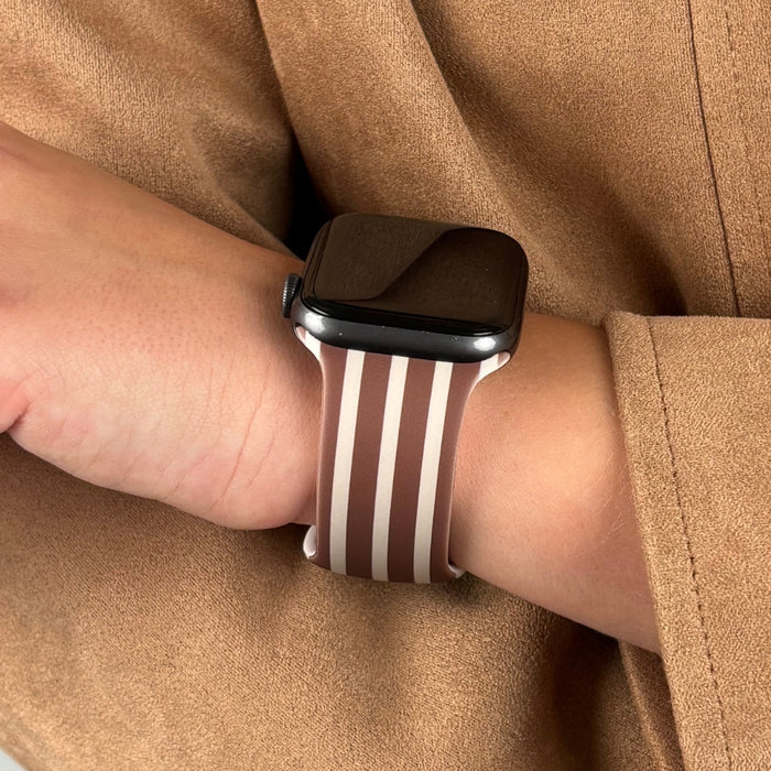 Coconut Lane Apple Watch strap with chestnut stripes, worn on a wrist with a beige sleeve.