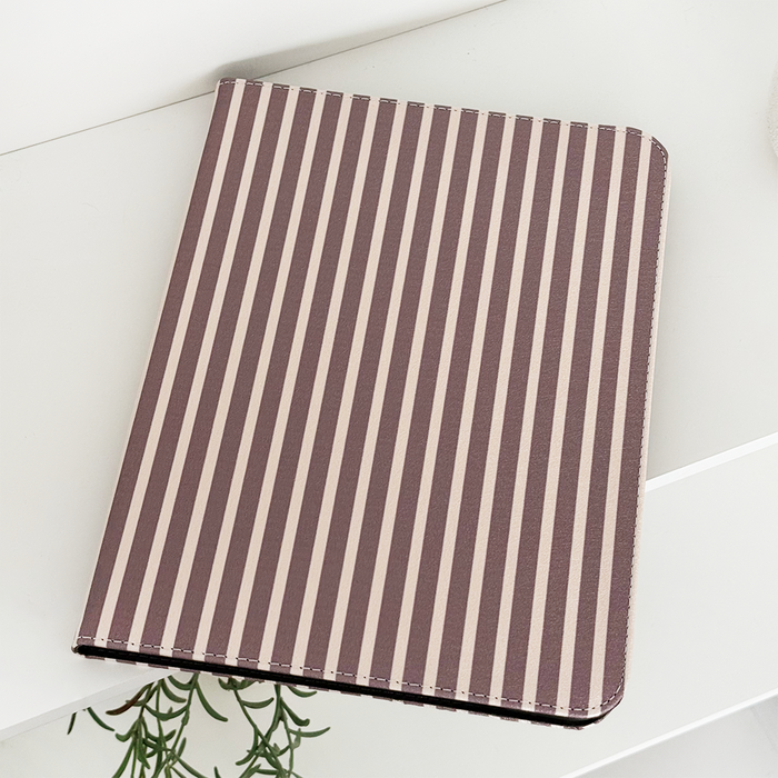 Chestnut Stripes iPad case in vegan leather on a white surface next to a green plant.