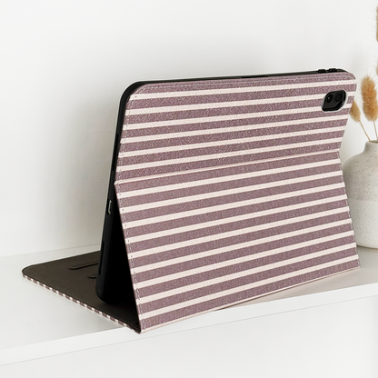 IPad in a Coconut Lane chestnut striped case on a white surface next to a vase of dried flowers.