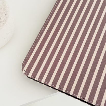 Brown and beige striped iPad case on a white surface next to a round, textured container.