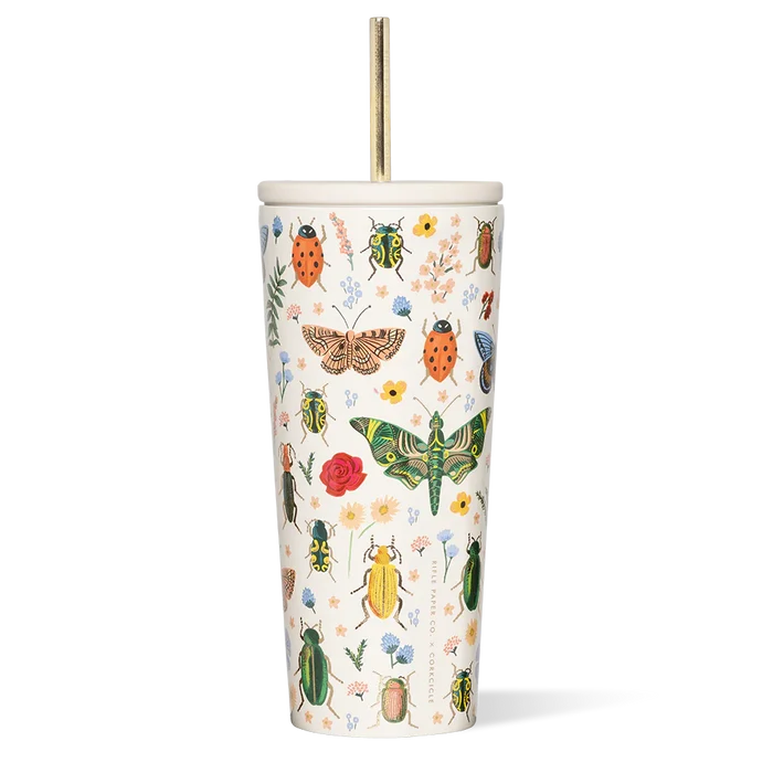 A tall white reusable straw cup with Rifle Paper Co's floral print, featuring various insects and flowers, paired with a gold-colored metal straw.