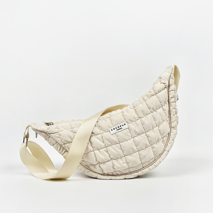 Beige quilted crossbody dog walking bag by Coconut Lane with a crescent shape and built-in poop bag dispenser.
