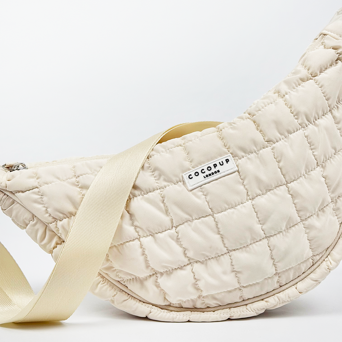 Cloud Crossbody Crescent Dog Walking Bag by Coconut Lane with a wide cream strap and front logo, shown on a white background.