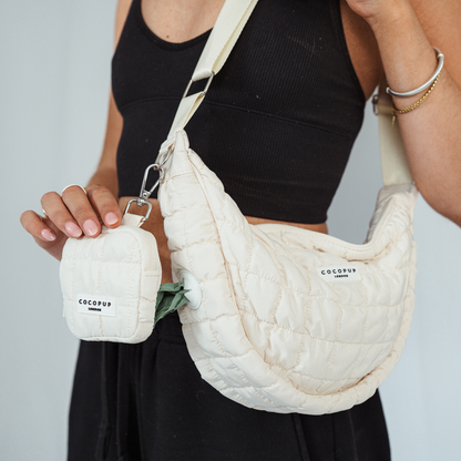 Person wearing a light grey Coconut Lane crossbody crescent dog walking bag with matching pouch.