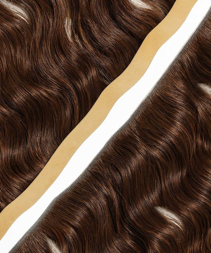 Two bundles of shiny, wavy brown hair extensions lie parallel with a white and beige strip between them; glossy, defined waves.