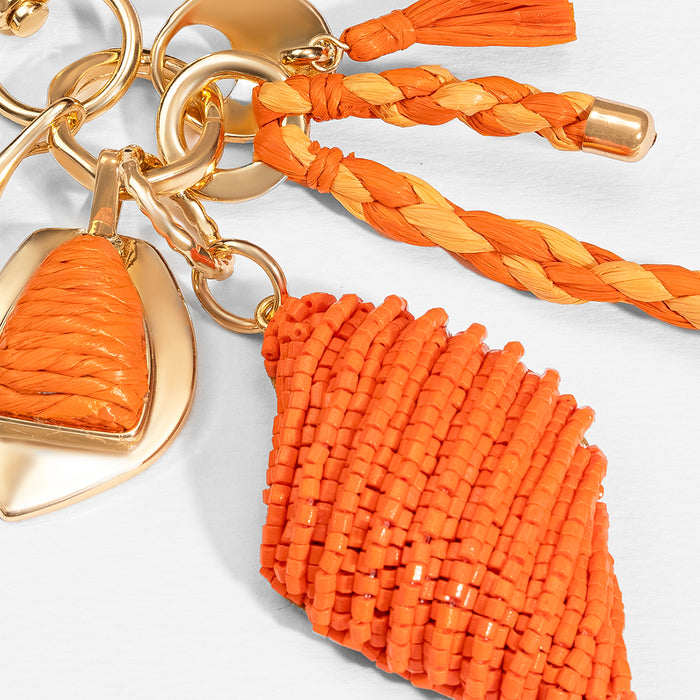 Vibrant orange bag charm with raffia tassels and beaded details, perfect for vacation vibes