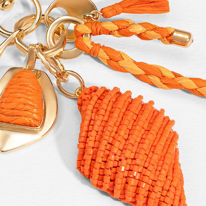 Vibrant orange bag charm with raffia tassels and beaded details, perfect for vacation vibes