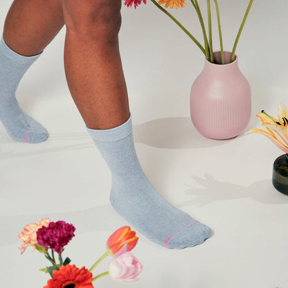 Light blue half cushion socks with pink accents, worn with flowers and vases in the background.