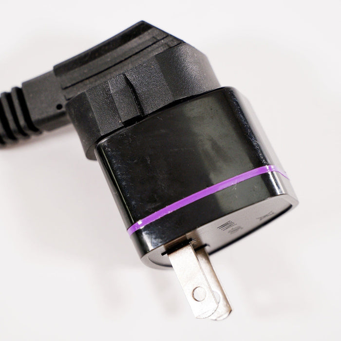Close-up of a black travel plug adapter with a purple band, two metal prongs, and an attached black cord on a white background.