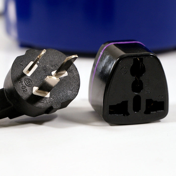 A black three-pronged electrical plug rests beside a universal travel adapter on a white surface, with a blurred blue device in the background.