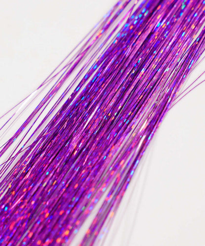 Close-up of several shiny Perfect Locks Perfect Hair Tinsel strands in Bubblegum, arranged diagonally on a white background. Reflective tinsel catches light with multicolored sparkles, resembling Remy hair extensions.#color_soft-purple