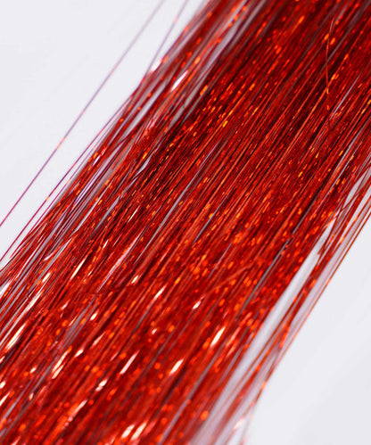 Close-up of many thin, shiny Hot Pink Perfect Hair Tinsel strands from Perfect Locks laid in parallel on a light background, resembling sparkling hair extensions as they reflect the light.#color_ruby-red