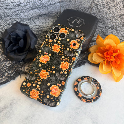Haunted Blossoms MagSafe grip ring lying beside the matching black gothic floral Wavy Luxe case on black spiderweb mesh.
