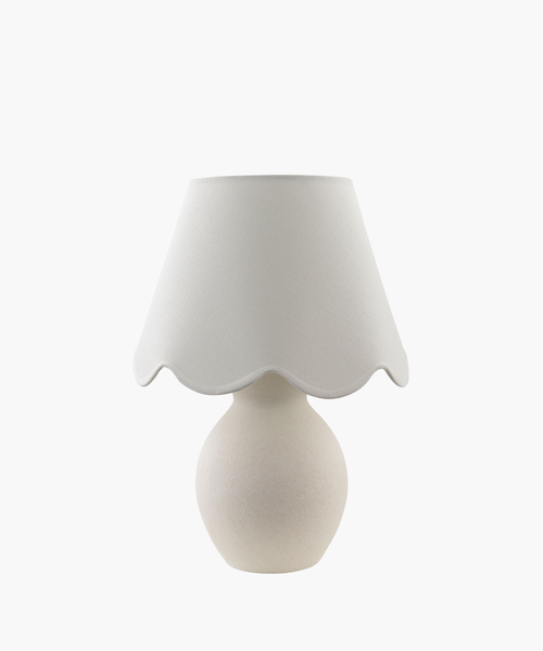 A cream-colored table lamp with a rounded base and a scalloped fabric shade, conveying a cozy and elegant feel. The design is minimalist and classic. | Wildwood Home Co.