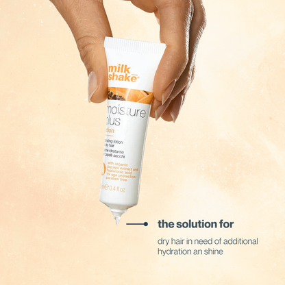 Hand holding a tube of milk_shake hair lotion against a beige background