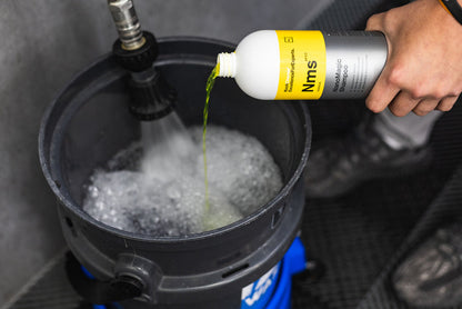 Person pouring NanoMagic Shampoo bottle into a black bucket with water