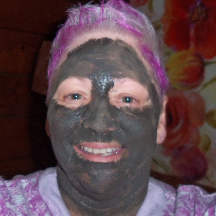 Woman with purple hair wearing organic charcoal face mask for glowing skin care routine