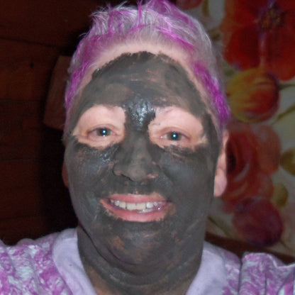 Woman with purple hair wearing organic charcoal face mask for glowing skin care routine