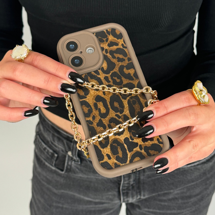 Hand with black nails holds a phone featuring a gold chain strap and leopard print case.