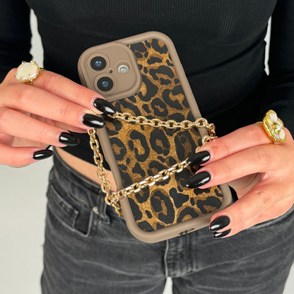 Hand with black nails holds a phone featuring a gold chain strap and leopard print case.