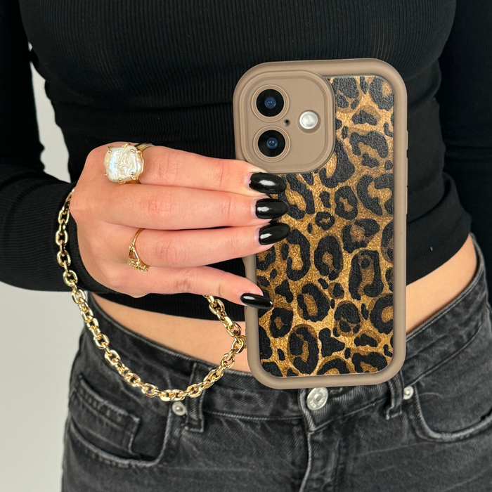 Leopard print phone case with Coconut Lane gold chain strap, held by person in black top, jeans, and gold ring.