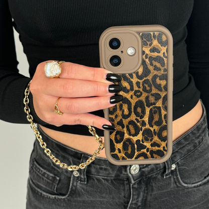 Leopard print phone case with Coconut Lane gold chain strap, held by person in black top, jeans, and gold ring.