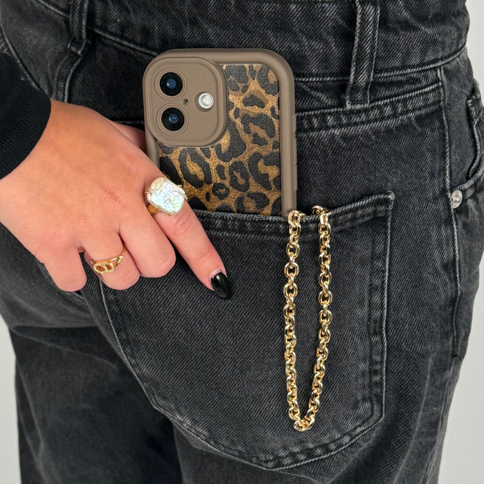 Gold chain phone strap from Coconut Lane attached to a phone, held by a hand with rings in a black jeans back pocket.