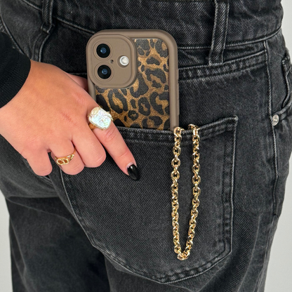 Gold chain phone strap from Coconut Lane attached to a phone, held by a hand with rings in a black jeans back pocket.