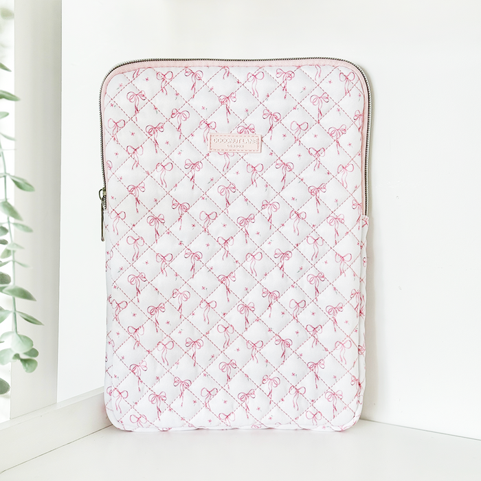 Quilted iPad sleeve with dainty bow pattern stands upright on a white surface near a window.
