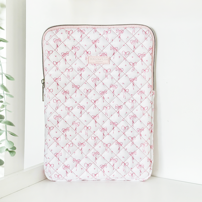 Quilted iPad sleeve with dainty bow pattern stands upright on a white surface near a window.
