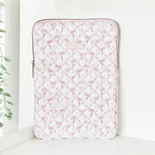 Quilted iPad sleeve with dainty bow pattern stands upright on a white surface near a window.