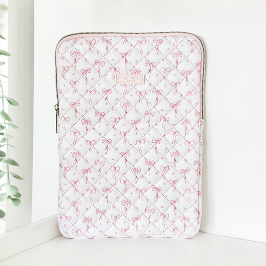 Quilted iPad sleeve with dainty bow pattern stands upright on a white surface near a window.