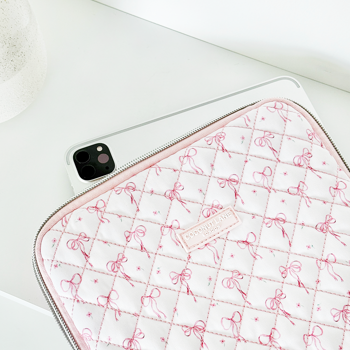 Quilted iPad sleeve with dainty bow pattern holds a tablet on a white surface, round object beside it.